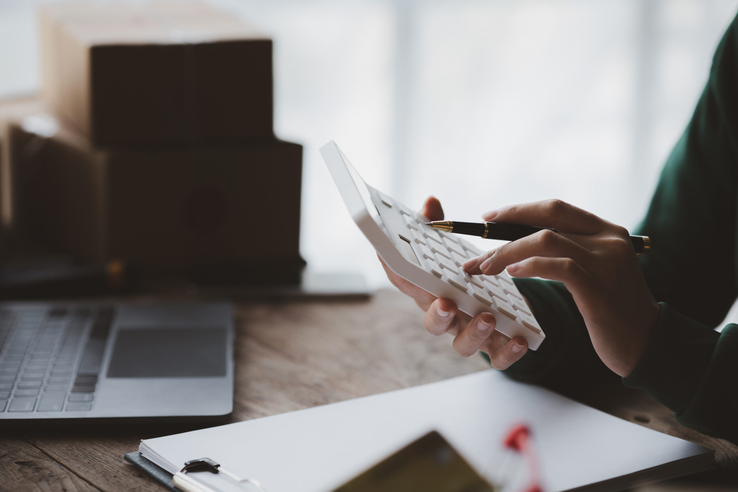 Product management | Immagine di un manager al lavoro in ufficio | Dettaglio delle mani e di una calcolatrice con un laptop sullo sfondo